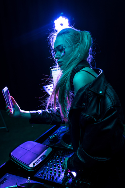 κομψό dj κορίτσι αγγίζει εξοπλισμό dj όταν λήψη selfie σε νυχτερινό κέντρο διασκέδασης  - Φωτογραφία, εικόνα