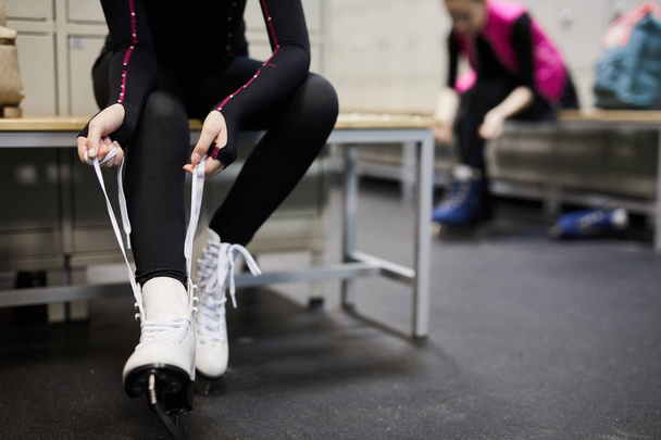 Retrato de seção baixa de mulher jovem irreconhecível amarrando sapato de patinação no vestiário antes da prática, espaço de cópia
 - Foto, Imagem