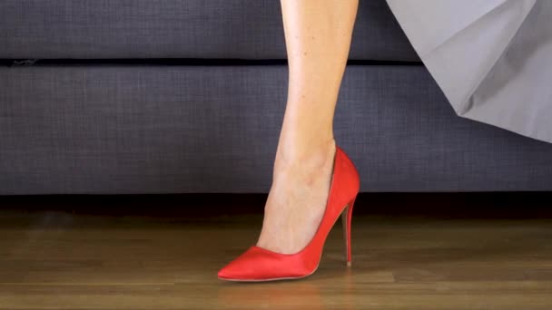 Γυναίκα στον καναπέ σε κόκκινα ψηλά τακούνια διασχίζει σέξι και Slim μακριά πόδια - Πλάνα, βίντεο