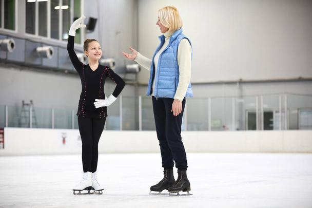 Retrato de comprimento total de patinação artística menina feliz na pista olhando para treinador feminino dando instruções durante o treinamento, espaço de cópia
 - Foto, Imagem