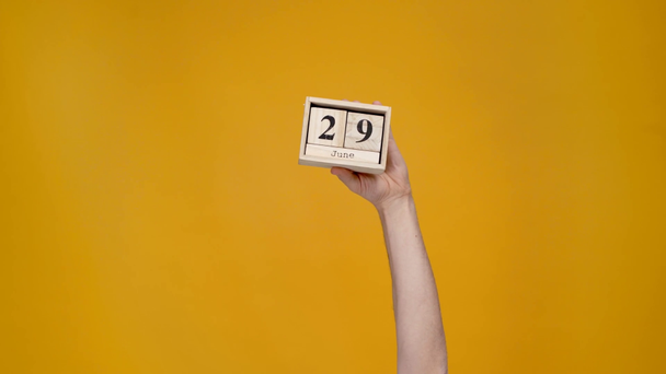 oříznutý pohled ženy představují dřevěné kalendáře s 29 června datum izolované na žluté - Záběry, video