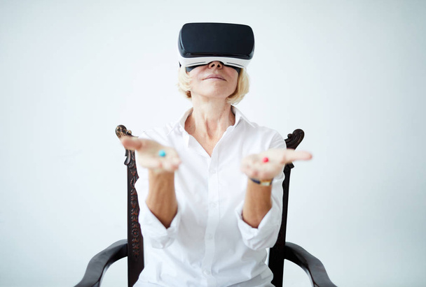 Muotokuva kypsä nainen yllään VR kuulokkeet ja tilalla kaksi eri pillereitä käsissä, kopioi tilaa
 - Valokuva, kuva
