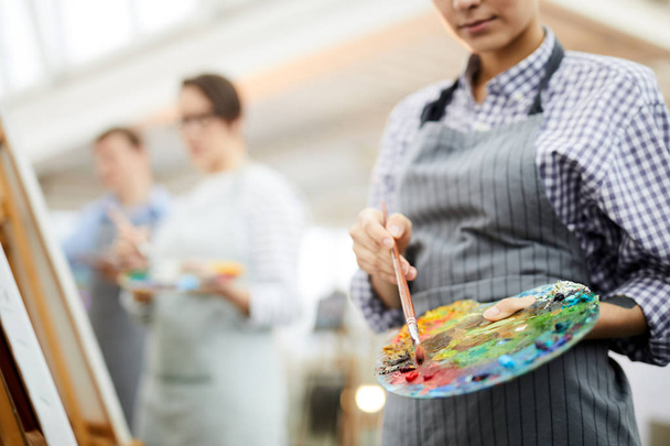 Mid sectie portret van onherkenbare vrouwelijke kunstenaar Holding palet mengen olie kleuren tijdens het schilderen foto op ezel in de kunststudio, kopieerruimte - Foto, afbeelding