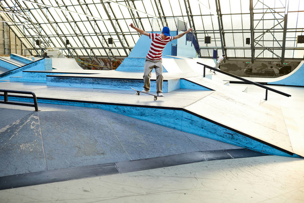 Хитрый активный мальчик в повседневной одежде стоит на скейтборде, двигаясь по плоской поверхности и собирается спуститься
 - Фото, изображение
