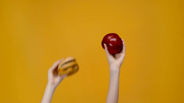 частичный взгляд женщины, представляющей гамбургер и яблоко изолированы на желтый
 - Кадры, видео