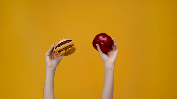 visão recortada de mulher apresentando hambúrguer e maçã isolada em amarelo
 - Filmagem, Vídeo
