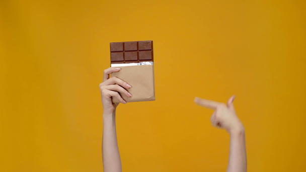 Ausgeschnittene Ansicht einer Frau, die Schokolade hält, mit dem Finger zeigt und Daumenhoch-Zeichen zeigt, isoliert auf gelb - Filmmaterial, Video
