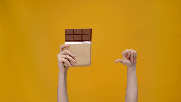 oříznutý pohled žena hospodářství čokolády, ukázal prstem a ukazuje palec dolů znamení izolované na žluté - Záběry, video