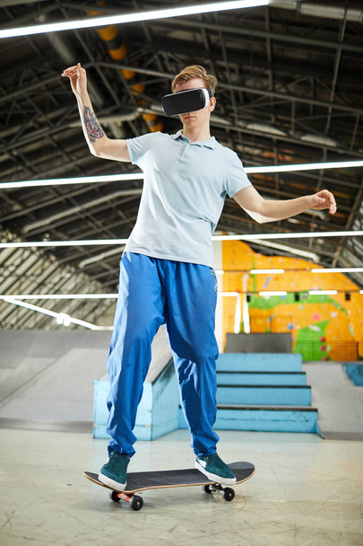 Aktiver Teenager mit vr-Headset, der auf dem Skateboard steht, während er auf Parkour trainiert und in der virtuellen Welt unterwegs ist - Foto, Bild