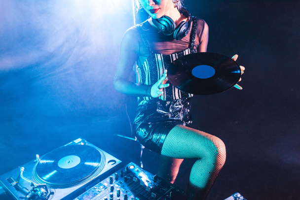 przycięte widzenia dj kobieta trzyma rekord retro winylu i stojący w pobliżu sprzętu dj w klubie nocnym z dymu  - Zdjęcie, obraz