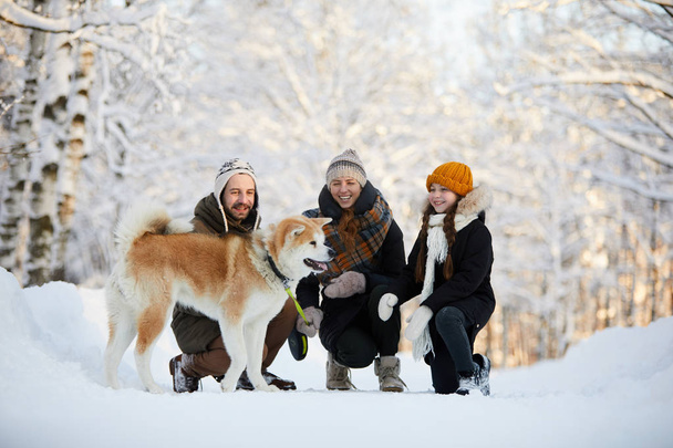 Täyspitkä muotokuva onnellinen perhe nauttii kävellä koiran kanssa kauniissa talvipuistossa, kopioi tilaa
 - Valokuva, kuva
