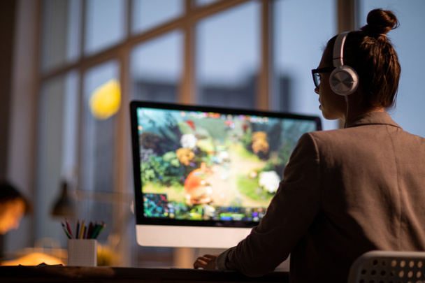 Jovem colorista ou editor de imagens em fones de ouvido sentado na frente do monitor de computador com vídeo na tela
 - Foto, Imagem