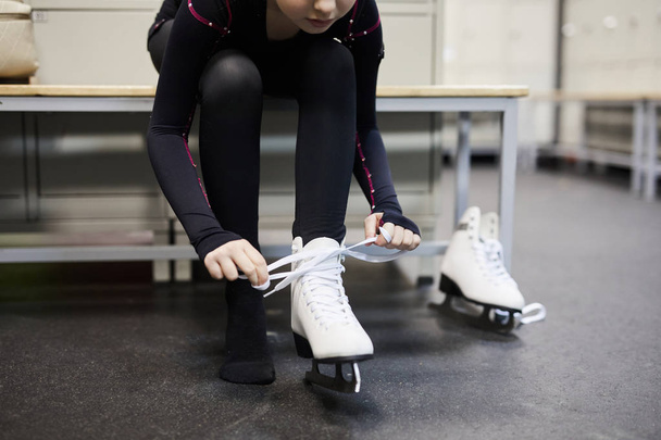 Retrato de sección baja de una chica irreconocible atando zapato de patinaje en el vestidor antes de la práctica, espacio para copiar
 - Foto, imagen
