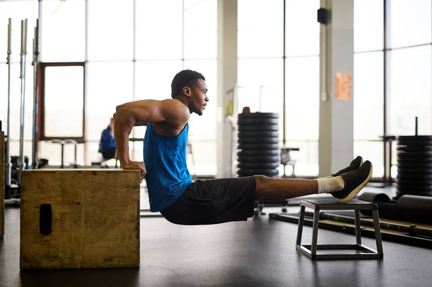 Jeune athlète afro-américain actif faisant de l'exercice sur un équipement de cross-training dans un centre de fitness ou une salle de gym
 - Photo, image