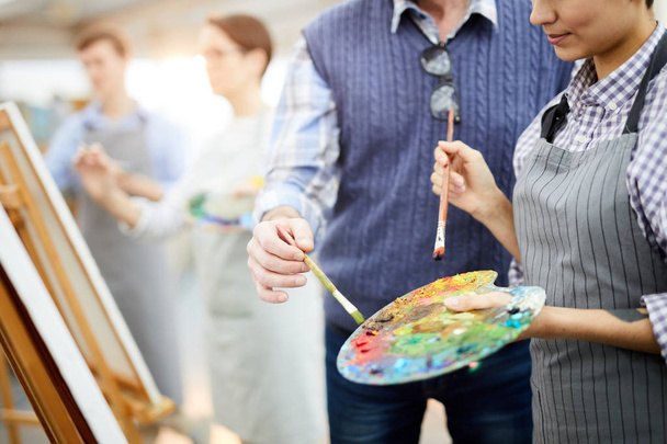 Mid section portrait of two unrecognizable artists holding palette mixing oil colors while painting picture on easel in art studio, copy space - Photo, Image