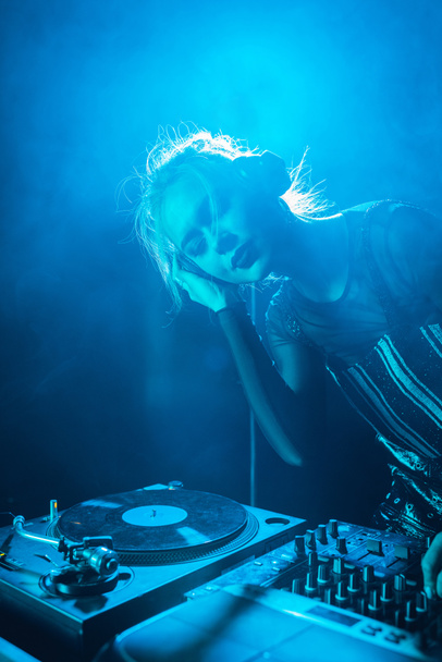 beautiful dj girl listening music in headphones while standing with closed eyes in nightclub with smoke  - Foto, Imagem