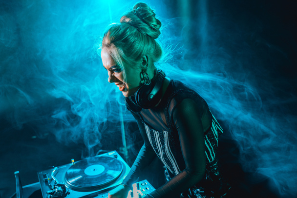 wütende blonde dj Mädchen mit dj Ausrüstung in Nachtclub mit Rauch  - Foto, Bild