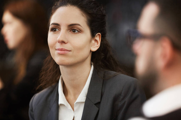 Mooie jonge brunette zakenvrouw zittend tussen collega's op training, seminar of conferentie - Foto, afbeelding