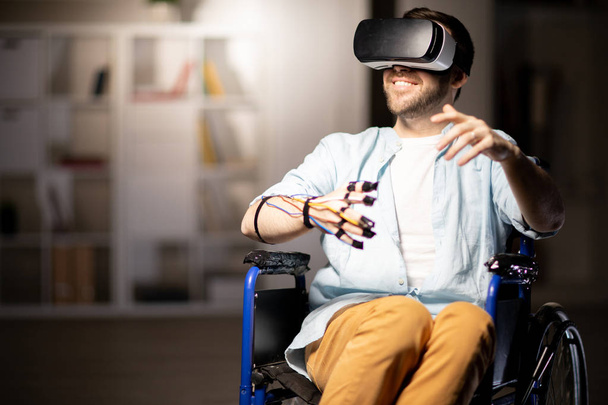 Junger fröhlicher behinderter Mann mit Sensoren und vr-Headset genießt virtuelles Abenteuer im Rollstuhl - Foto, Bild