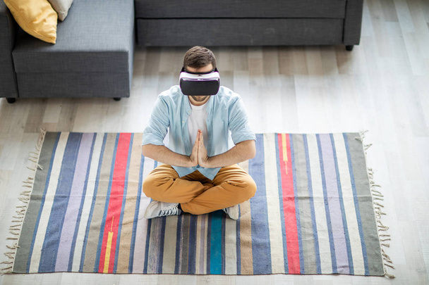 Young man in casualwear keeping his hands put together in front of chest while watching yoga stuff in vr headset - Photo, Image