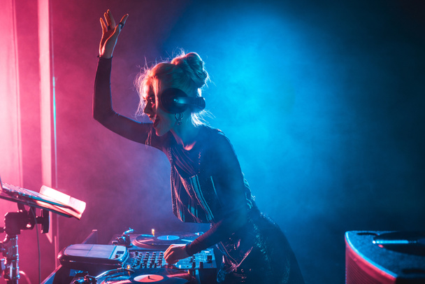 feliz dj chica con rubia pelo usando dj mixer en nightclub con humo
 - Foto, Imagen