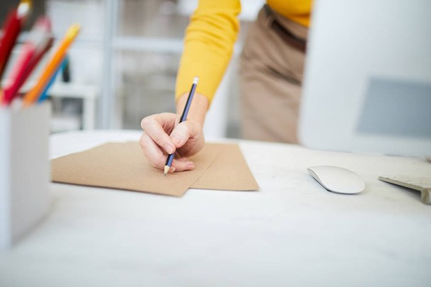 Closeup of unrecognizable businesswoman writing note on craft paper at workplace, copy space - Photo, Image