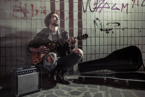 Вуличний музикант грає на гітарі в метро. Вагрантський спосіб життя. Гра в підвалі, щоб заробляти на життя. Безробітний музикант. Майбутня рок-зірка
. - Фото, зображення