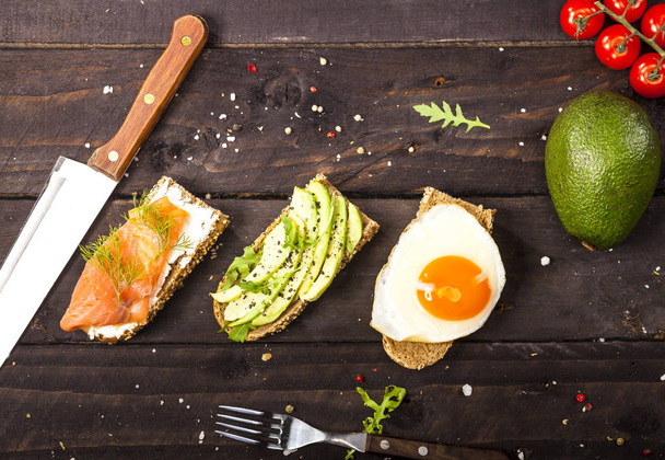 Three different bruschettas with avocado, rucola sesame, seeds, egg, salmon on wooden table - Foto, afbeelding