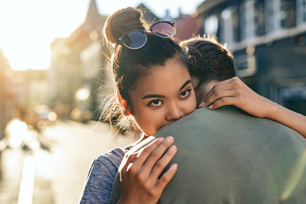 Young woman hugging her boyfriend while standing together on a city street in the late afternoon - 写真・画像