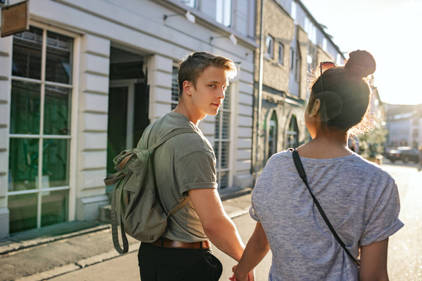 Smiling young man looking over his shoulder while walking hand in hand with his girlfriend on a city street in the afternoon - Fotografie, Obrázek