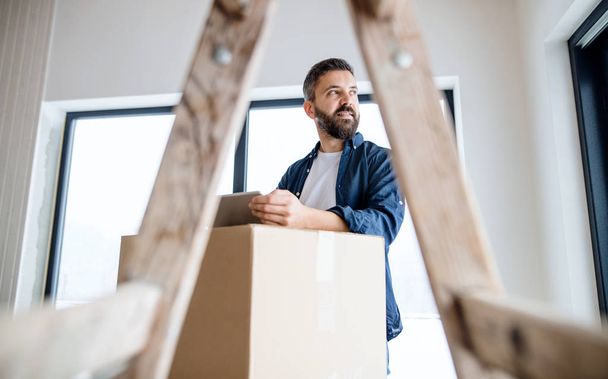 A mature man with tablet and cardboard boxes furnishing new house. - Fotoğraf, Görsel