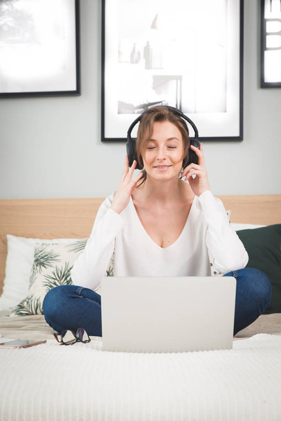 Girl in plaid listening music in headphones, sitting on sofa. - Zdjęcie, obraz