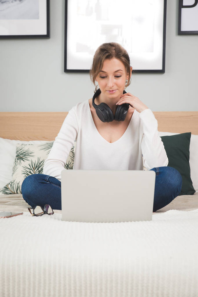 Girl in plaid listening music in headphones, sitting on sofa. - Фото, изображение