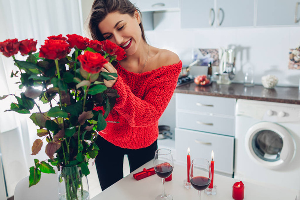Młoda kobieta znaleziono czerwone róże z świec, wina i dar pole na kuchnia. Szczęśliwa dziewczyna pachnące kwiaty. Dzień kobiet - Zdjęcie, obraz