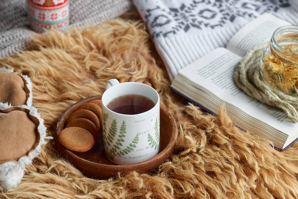 Уютный домашний натюрморт: чашка чая и открытая книга с теплой клеткой. Зимние праздники, Рождество
 - Фото, изображение