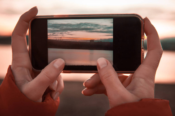 Mujeres manos sosteniendo un teléfono móvil con una foto del paisaje con la montaña y el lago
. - Foto, Imagen