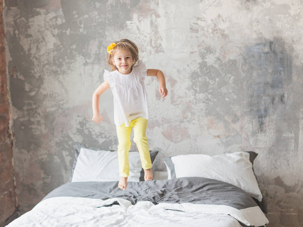 Happy child girl having fun jumping on a bed - 写真・画像