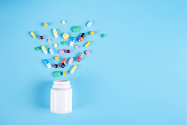 Pílulas coloridas, comprimidos e garrafa branca em fundo azul
 - Foto, Imagem