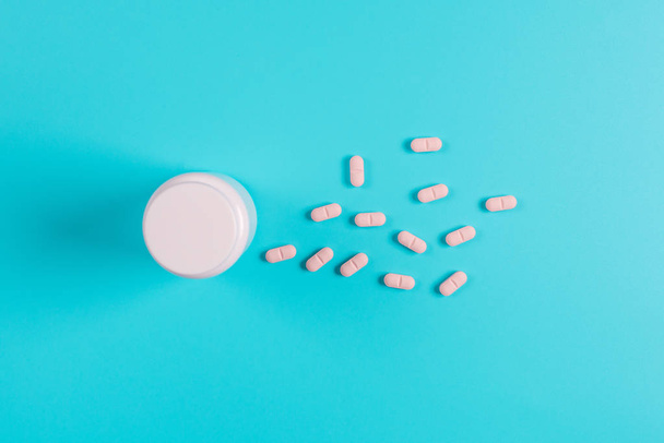 Růžový prášky, tablety a bílá láhev na modrém pozadí - Fotografie, Obrázek