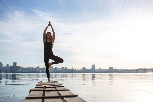 Young woman practicing yoga exercise at quiet wooden pier with c - Foto, Imagem