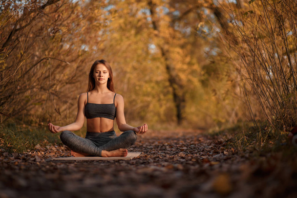 Young woman practicing yoga exercise at autumn park with yellow  - Фото, изображение