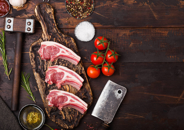 Fresh raw butchers lamb beef cutlets on chopping board with vintage meat hatchet and hammer on wooden background.Salt, pepper and oil with tomatoes and garlic and barbeque sauce. Space for text - Foto, Bild