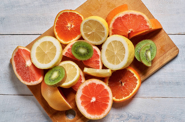 Limões, laranjas, toranjas e kiwi fatiados em um prato de madeira
. - Foto, Imagem