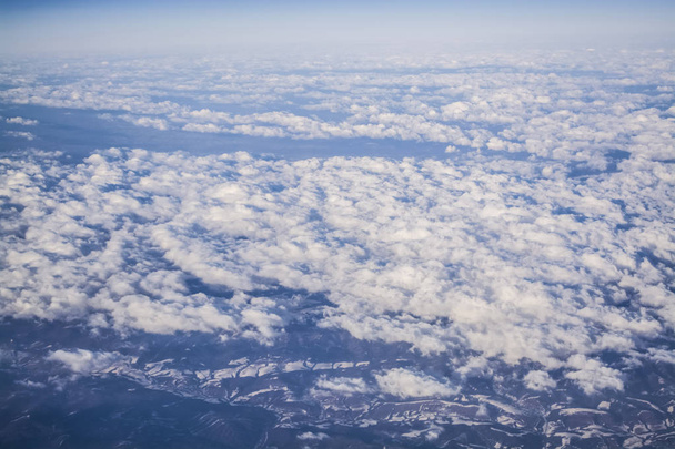 View from a plane window on clouds and blue clear sky and the earth from height. Beautiful view from air of mountains.  - Photo, Image