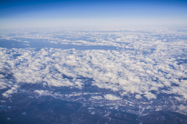 Blick aus einem Flugzeugfenster auf Wolken und blauklaren Himmel und die Erde aus der Höhe. schöne Aussicht aus der Luft auf die Berge.  - Foto, Bild