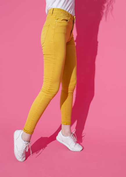 Female feet in trendy yellow jeans and white sneakers on a pink background - Foto, immagini