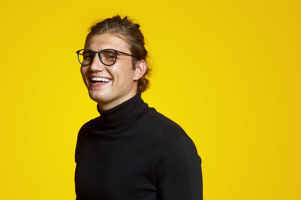 Retrato de cerca de un joven alegre guapo con cuello de polo negro y gafas que ríen alegres sobre el fondo amarillo
 - Foto, imagen