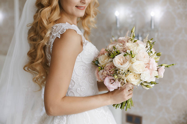 Hermosa novia rubia joven con estilo peinado de boda en un vestido de moda blanco con un ramo de flores en sus manos
 - Foto, imagen