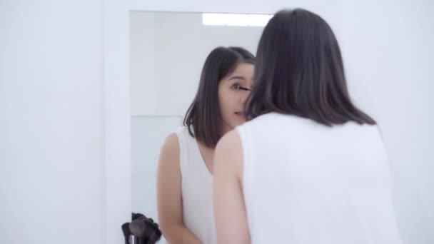 schöne asiatische Frau mit Wimpernzange Make-up vor dem Spiegel, glückliche Frau mit Schönheitskosmetik, um sich bereit zu verbessern, im Schlafzimmer zu Hause zu arbeiten. Lifestyle-Frauen entspannen sich zu Hause. - Filmmaterial, Video