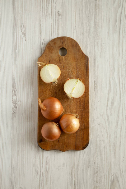 Neoloupané syrové organické zlaté cibule na dřevěné desce nad bílou wo - Fotografie, Obrázek